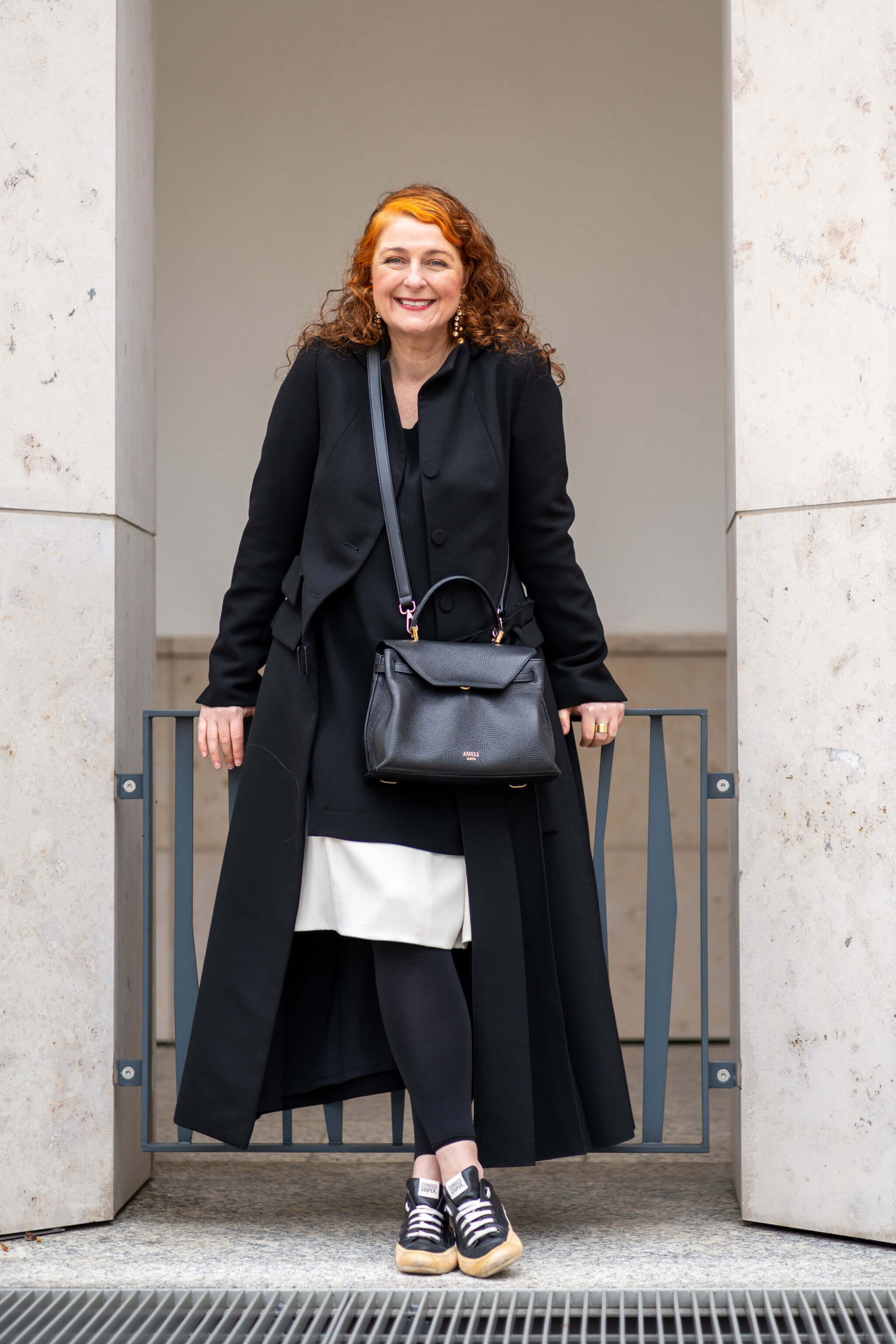 Cerstin Henning trägt ein Outfit von Annette Görtz mit Mantel und Kleid in Schwarz-Creme, Sneakers von Candice Cooper und Tasche von Ameli Zurich – stilvolle Modeinspiration für Frauen über 50.