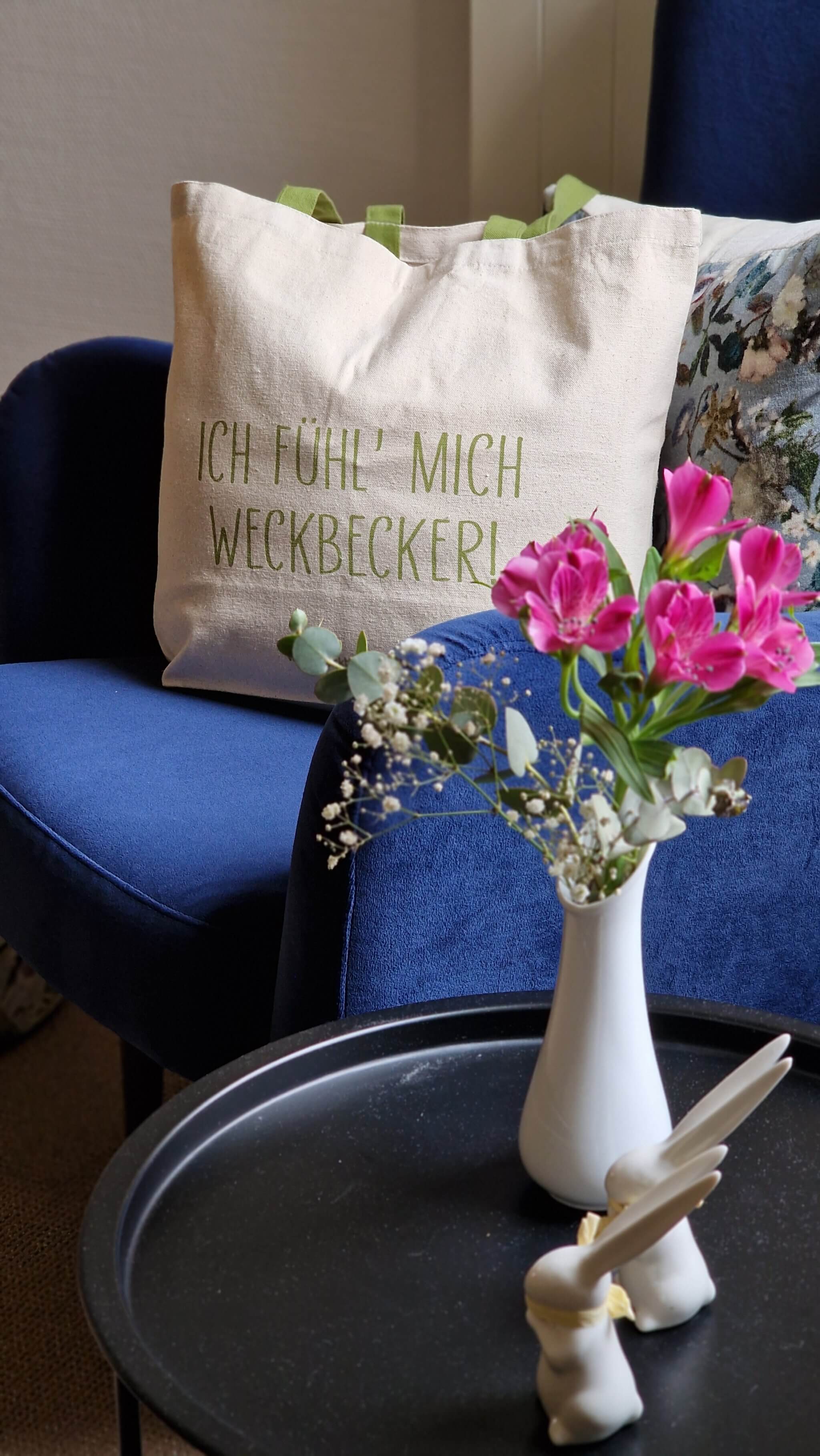 Detailaufnahme aus der Weckbecker Klinik Bad Brückenau: Blumen, ruhige Lounge-Atmosphäre und Tasche „Ich fühle mich Weckbecker“ – stilvolle Umgebung für Heilfasten, Entschleunigung und ganzheitliche Erholung