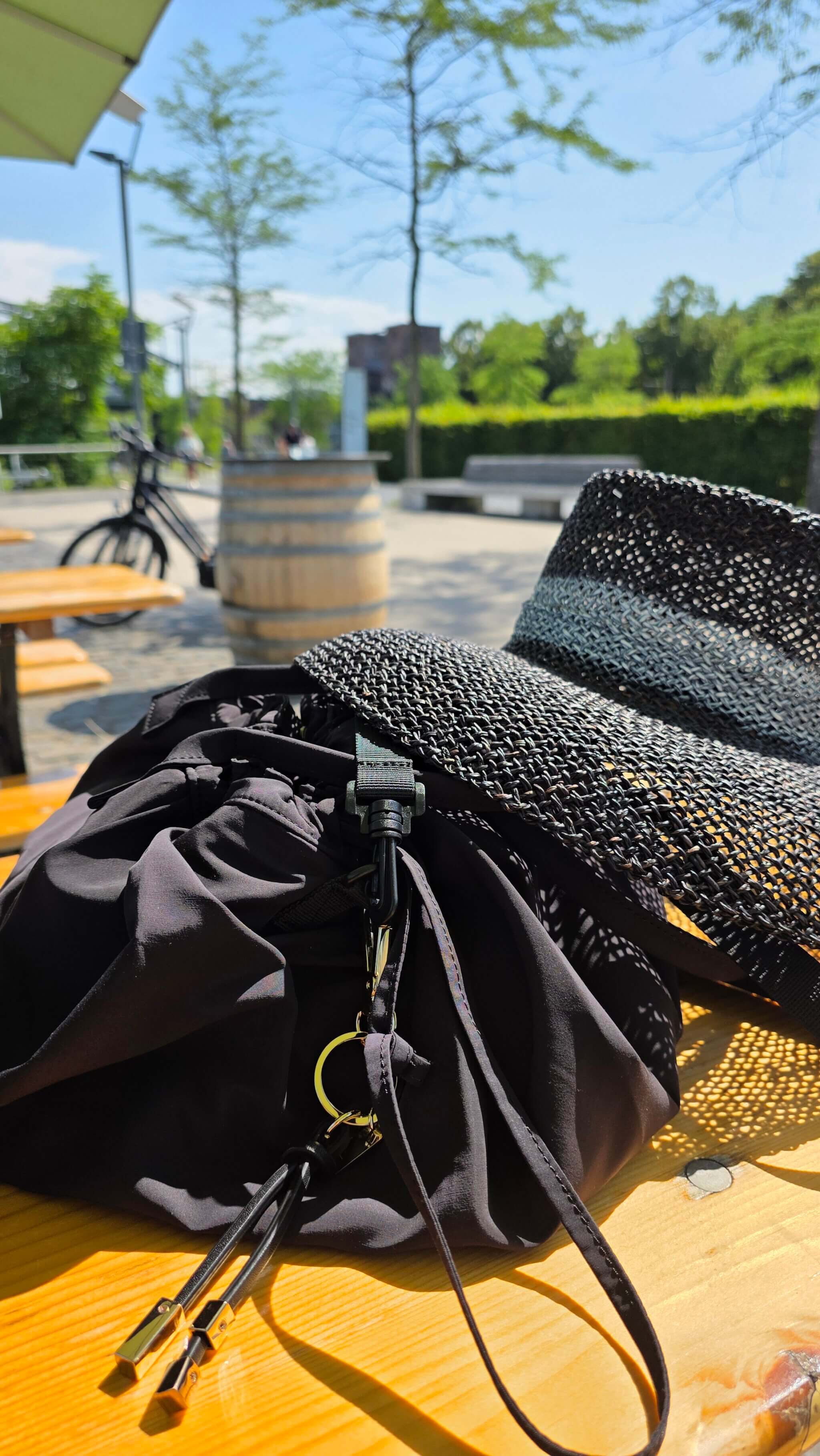 Schwarze Reisehandtasche aus der Uniqlo : C Kollektion, als Crossbody getragen, Dunkle Reisehandtasche aus der Uniqlo : C Kollektion, mit goldenem Anhänger von Maison Heroine 